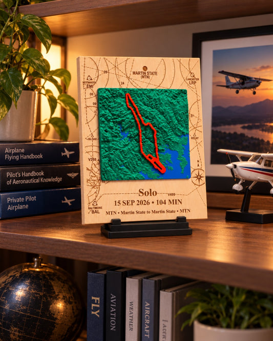 First solo flight keepsake with raised 3D terrain and red flight route displayed on a shelf with pilot handbooks and model airplane